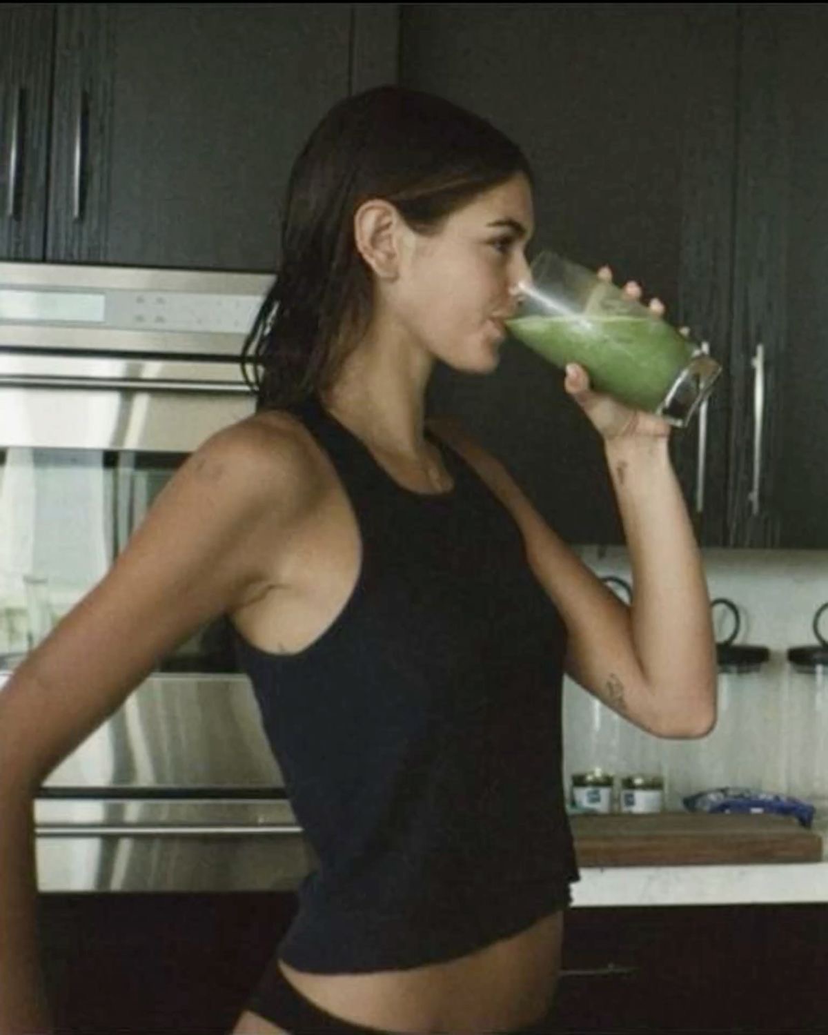 Woman drinking a green juice in a dark modern kitchen