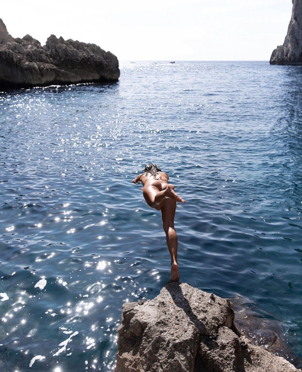 Woman balancing on a rock before diving into a clear Mediterranean cove