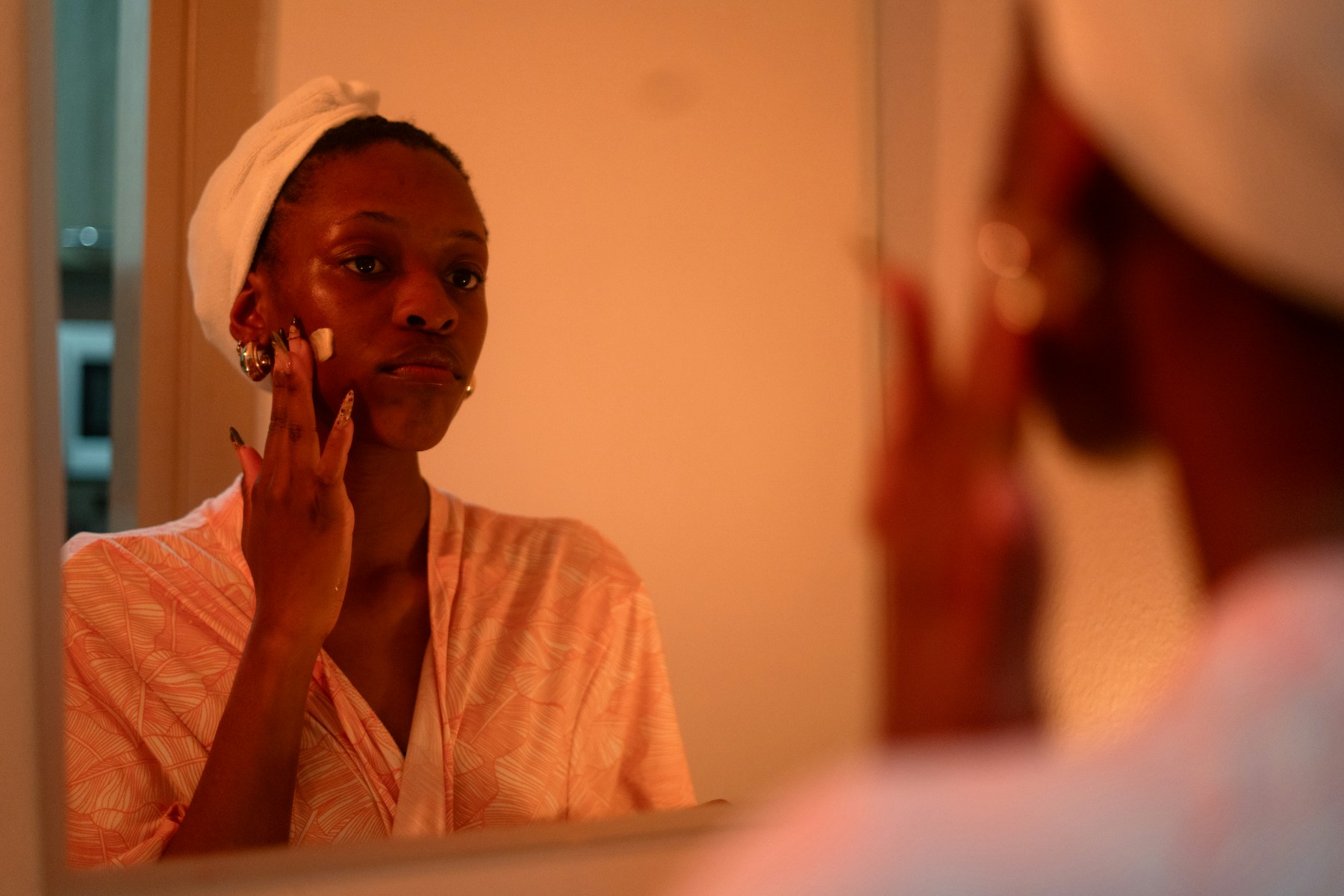 A woman applying face cream in warm light before a mirror