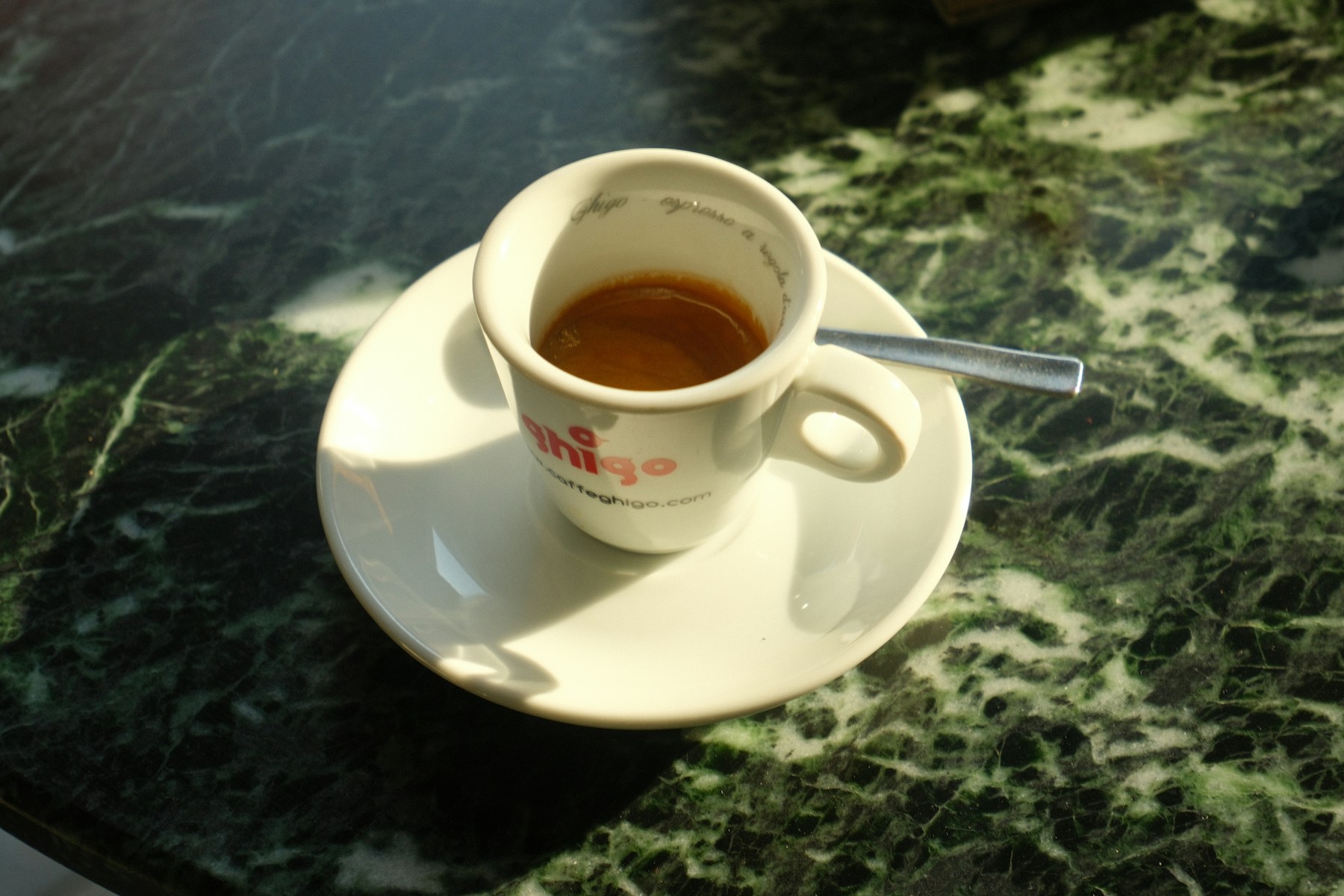 A small espresso cup casting a shadow on green marble